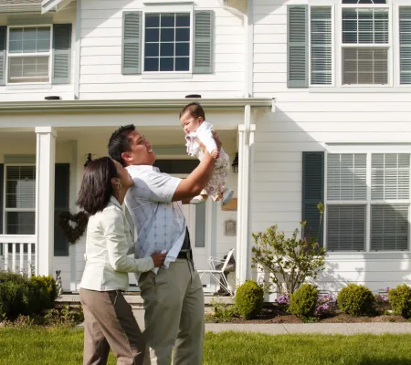 A couple holding a baby in front of a two-story home